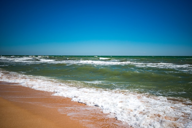 Waves of a noisy sea with blue water splashing on a sandy beach on a sunny warm summer day