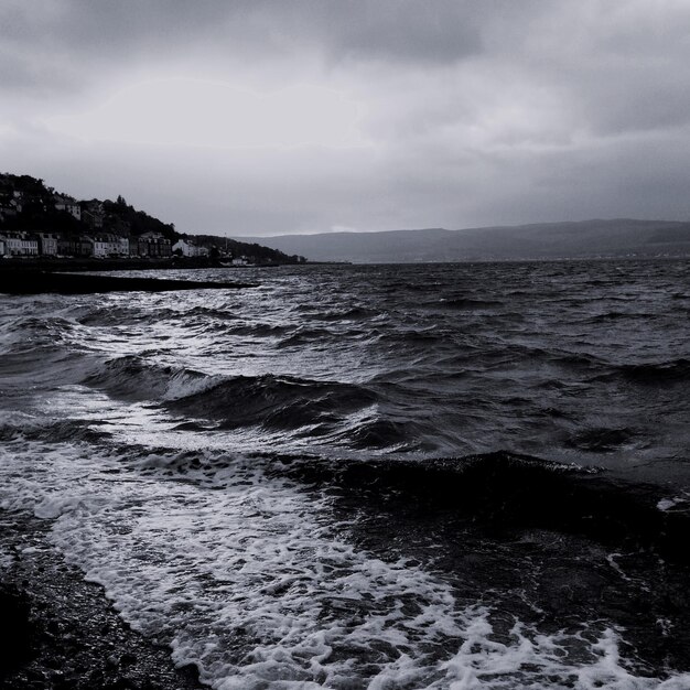 Waves rushing towards beach against sky