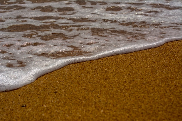 Foto onde sulla costa del mare, spiaggia sabbiosa. schiuma sull'acqua di mare.
