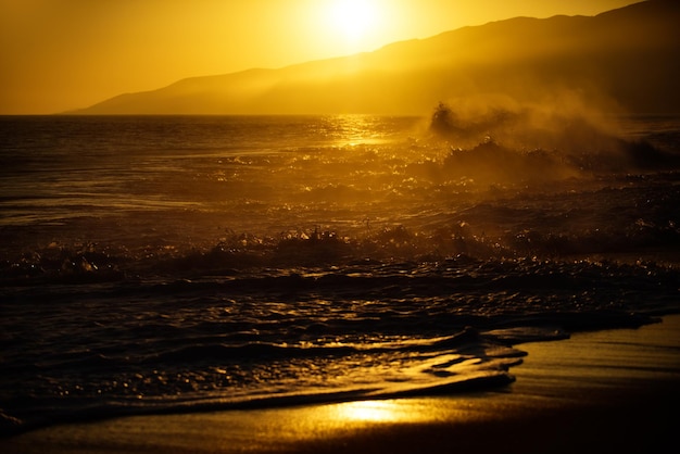 Waves splashes gold sky and ocean water sunset with large yellow sun under the sea surface