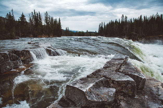 Waves and splashes of mountain river on background of forest and dramatic sky