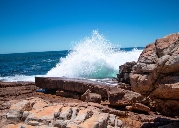 Waves splashing on rocks at shore against clear sky