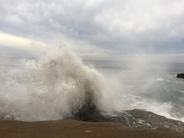 Photo waves splashing on rocks at shore against cloudy sky