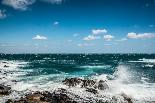 Waves splashing on rocky shore against sky