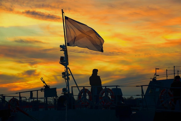 Waving flag of the navy on a warship against the backdrop of sunset