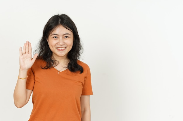 Gesto di saluto della mano d'ondeggiamento di bella donna asiatica che indossa maglietta arancione isolata su white