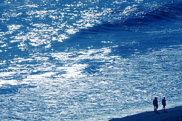 Wavy blue sea with silhouette of a group of people walking along the beach