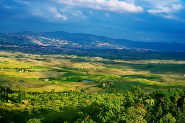 Wavy fields in Tuscany with shadows and farms Italy Natural outdoor seasonal spring background with blue sky and clouds