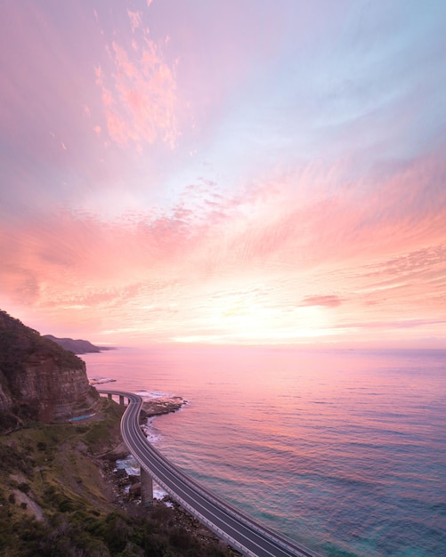 Photo wavy road between mountain and sea under cloudy sky