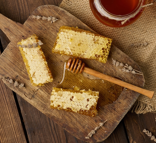 Wax bee honeycomb with honey on wooden board and wooden spoon, brown table, top view