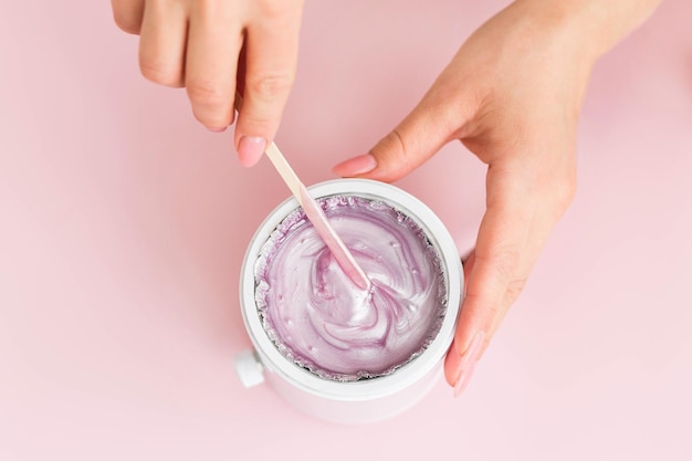 Wax melter wax heater wax melting device on a pink background Salon equipment Wooden spatula in female hands Pink wax Top view Close up