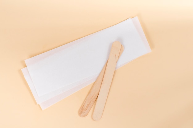 Wax strips for epilation and wooden sticks on beige background