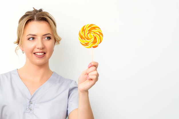 Waxing depilation concept The beautician is wearing a medical coat holding a sugar lollipop on white background