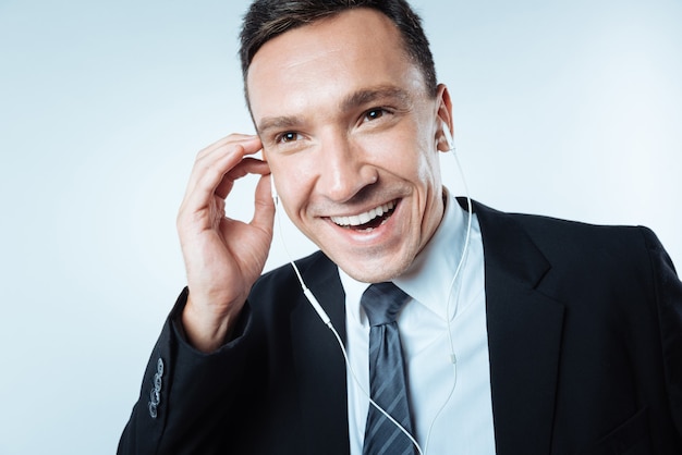 Way to relax. Happy cheerful delighted man smiling and holding headphones while enjoying his music