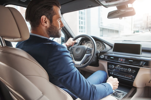 On the way to success confident and handsome young businessman in full suit is driving