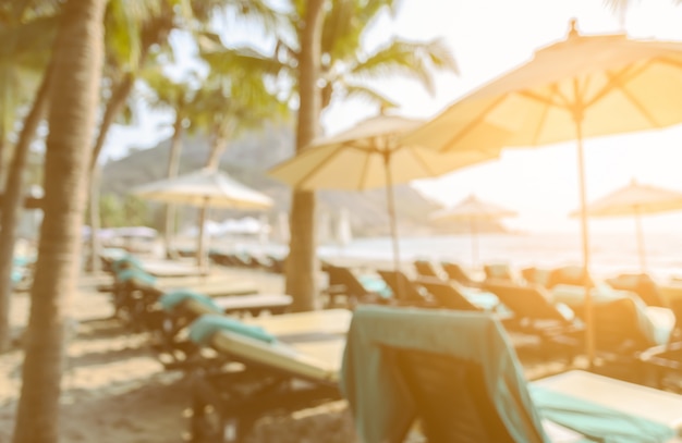 Wazig beeld van de achterkant van ligbedden en parasol op een tropisch strand met kokosnoot tress