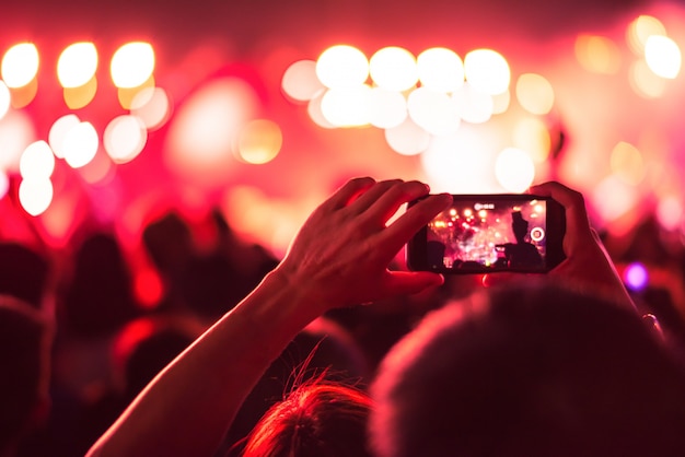 wazig kleurrijke achtergrond van hand met slimme telefoon tot het nemen van foto mensen druk in concert.