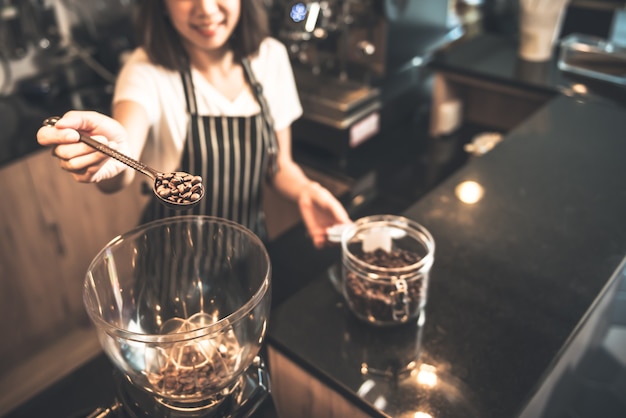 Wazig portret van een Aziatische vrouw barista Scooping gebrande koffiebonen in een koffiemolen