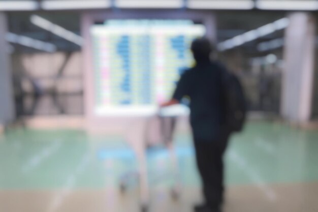 Wazig van de achterkant van een passagier die naar het vertrekdisplay kijkt en de vlucht op de luchthaven controleert.