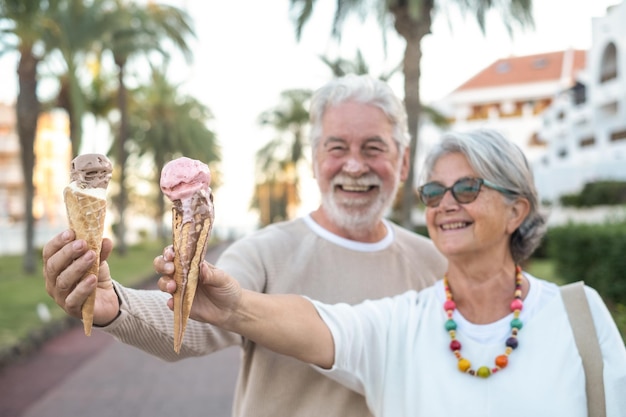 Wazig zicht op een glimlachend gepensioneerd echtpaar dat geniet van het eten van een ijsje in het park. Focus op het ijs dat aan het smelten is. Vrolijke bejaarde levensstijl concept.