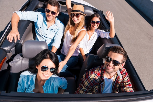 We always travel together. Top view of young happy people enjoying road trip in their white convertible and raising their arms