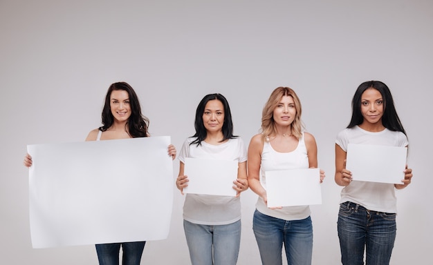 We are all human. Wonderful attractive fearless ladies standing close to each other and holding blank posters while posing