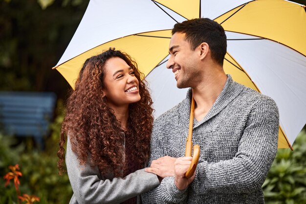 私たちは一緒に嵐を乗り越えることができます傘を持って雨の中に立っている若いカップルのショット