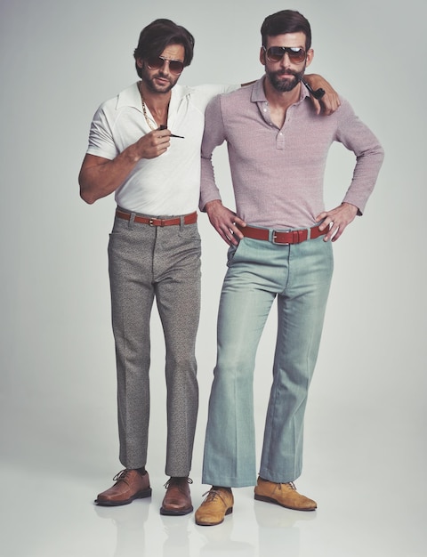 We doesnt always afraid of anything, but when we do, we doesnt afraid of anything. Studio shot of two men standing together while wearing retro 70s wear and smoking pipes.