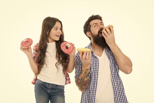 Foto abbiamo passione per le ciambelle gustose padre e figlia mangiano ciambelle vetrate uomo barbuto e bambina bambino che tiene ciambelle anello hipster e bambino carino con ciambelle fritte nelle mani