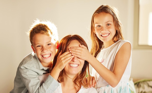 We hebben een verrassing voor je Foto van twee schattige kinderen die een band met hun moeder hebben thuis en haar ogen bedekken om haar te verrassen