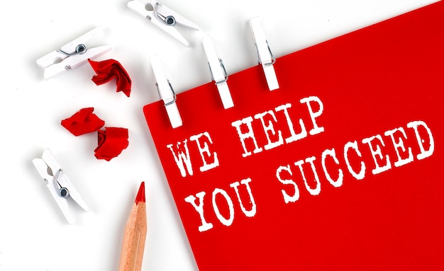 WE HELP YOU SUCCEED text on the red paper with office tools on white background