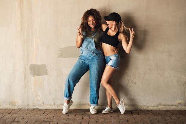 We know how to have fun Portrait of two cheerful young women posing for for a photo while leaning against a wall outside during the day