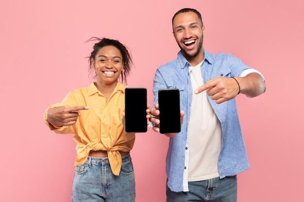 우리는 이 앱을 좋아합니다 행복한 커플이 검은 화면이 있는 두 대의 스마트폰을 보여주어 장치를 가리키는 모의를 합니다.