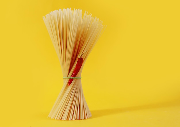 We love to cook deliciously long spaghetti a pod of red pepper on a yellow background a place for dough
