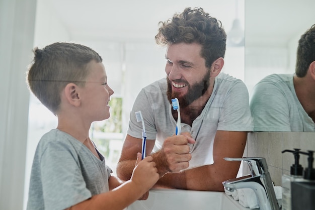 We mogen ons gebit verzorgen shot van een vader en zijn zoontje die samen hun tanden poetsen in de badkamer thuis