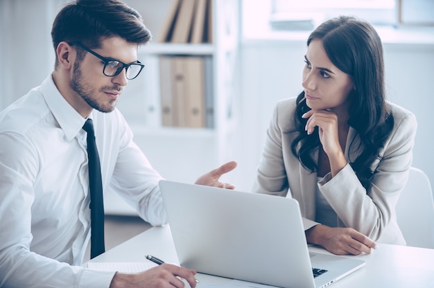 Dobbiamo cambiare questi numeri. due colleghi che discutono di qualcosa e usano il laptop mentre sono seduti al tavolo dell'ufficio