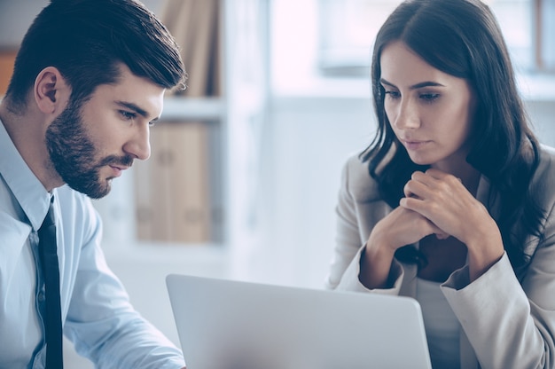 We need to read our contract once again. Close-up of beautiful young businesswoman looking at her laptop while sitting at the office table with her coworkers