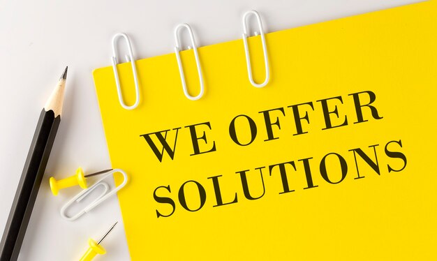 WE OFFER SOLUIONS word on yellow paper with office tools on the white surface