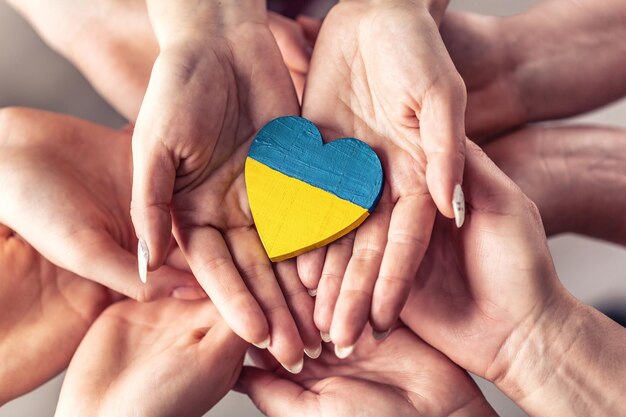 Фото Мы стоим с символом украины, когда многочисленные руки держат друг друга в единстве с деревянным сердцем, нарисованным в цветах украинского флага.