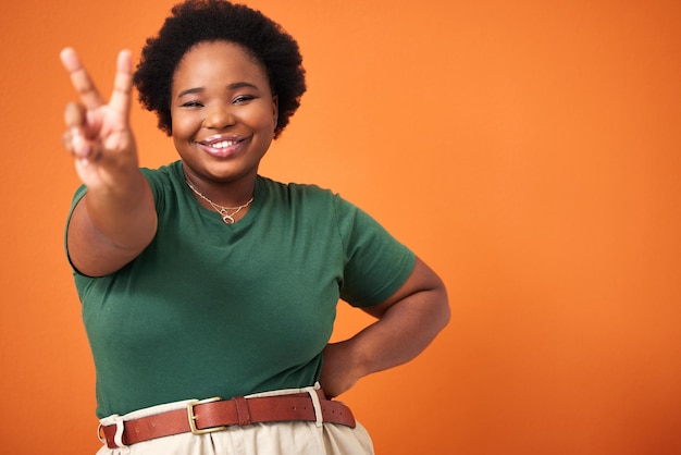 We verspreiden hier vrede en positiviteit. Shot van een mooie jonge vrouw die het vredesteken laat zien terwijl ze tegen een oranje achtergrond staat