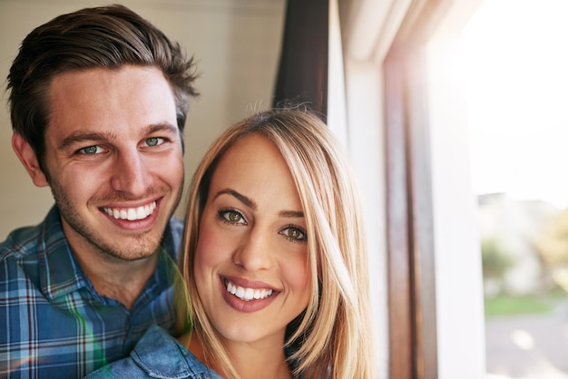 We vonden liefde Bijgesneden portret van een aanhankelijk jong stel dat voor een raam in hun huis staat