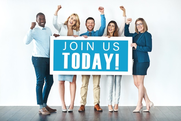 Photo we want you on our team studio shot of businesspeople holding up a sign with the words join us today on it and cheering