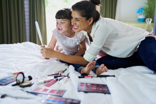 We zien er zo mooi uit Foto van een moeder en haar dochtertje die thuis met make-up op bed spelen