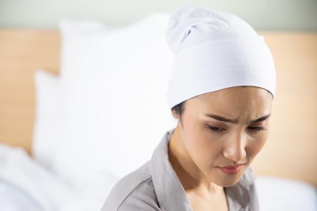 Weak asian woman cancer patient wearing head scarf after suffering serious hair loss and pain due to chemotherapy