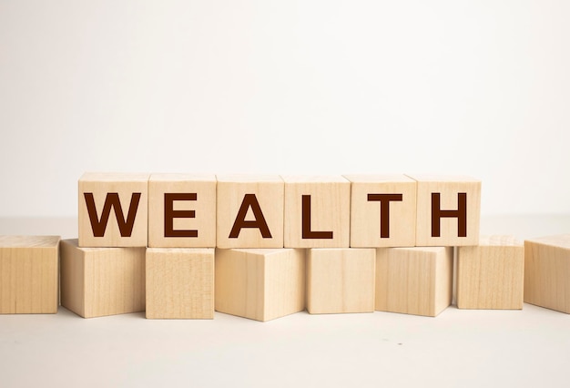 WEALTH라는 단어가 있는 배경 블록에 꽃이 있는 큐브 블록의 나무 책상에 있는 WEALTH 메시지 단어