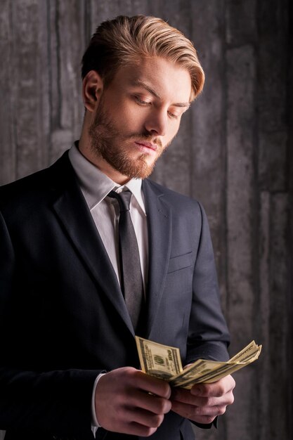 Wealthy handsome. Handsome young man in formalwear counting money