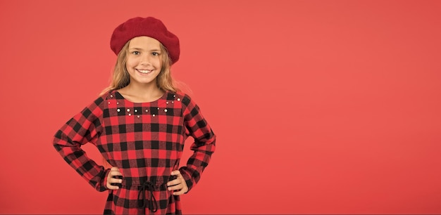 Wear beret like fashion girl Kid little cute girl with long blonde hair posing in beret hat and checkered dress red background Beret style inspiration Fashionable beret accessory for female