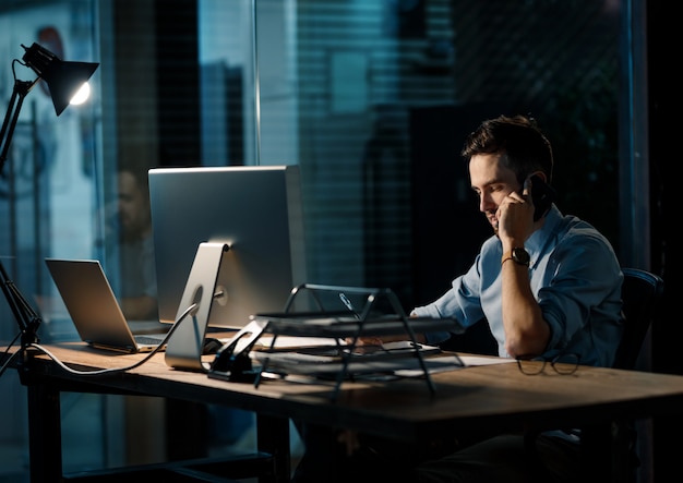 Уставший мужчина разговаривает по телефону в темном офисе
