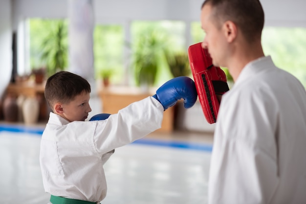 Wearing blue gloves. Dark-haired boy wearing blue gloves practicing punches with his aikido trainer