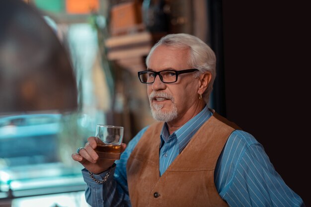 Wearing ear ring. Bearded retired man wearing ear ring drinking whisky alone in the bar